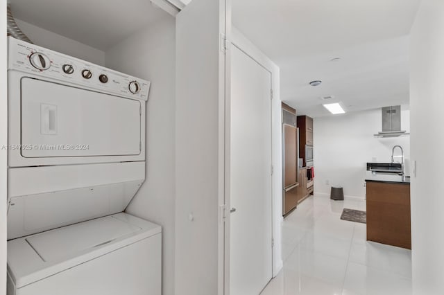 laundry area featuring laundry area, baseboards, stacked washing maching and dryer, a sink, and light tile patterned flooring