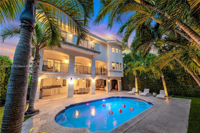 pool at dusk with area for grilling and a patio