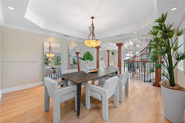 dining room with ornamental molding, a raised ceiling, light hardwood / wood-style flooring, and ornate columns