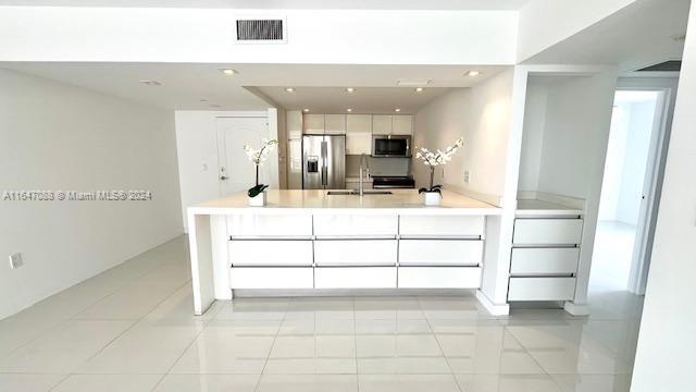 kitchen featuring sink, light tile patterned floors, stainless steel appliances, kitchen peninsula, and white cabinets