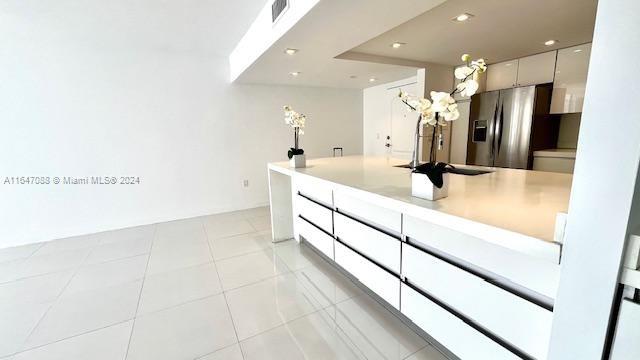 kitchen with white cabinetry, stainless steel fridge with ice dispenser, light tile patterned floors, and sink