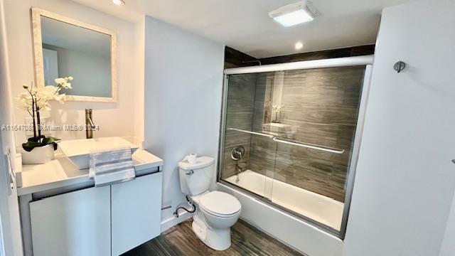 full bathroom featuring wood-type flooring, toilet, vanity, and enclosed tub / shower combo