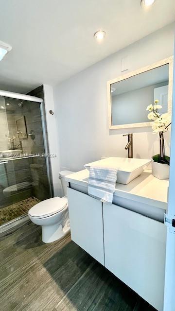 bathroom featuring a shower with door, toilet, vanity, and wood-type flooring