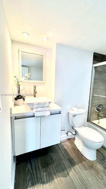 full bathroom featuring shower / bath combination with glass door, toilet, vanity, and hardwood / wood-style flooring