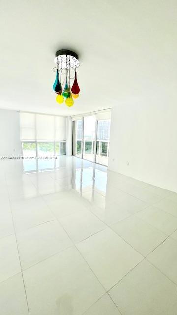 tiled empty room with expansive windows and a notable chandelier