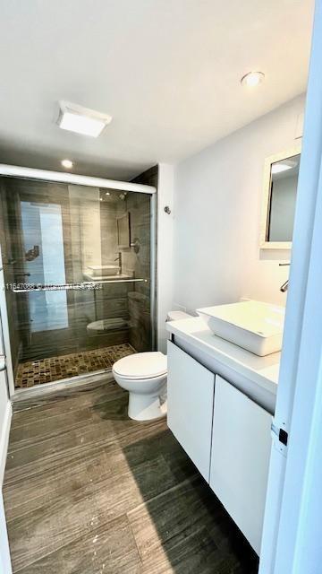 bathroom with wood-type flooring, toilet, vanity, and a shower with shower door