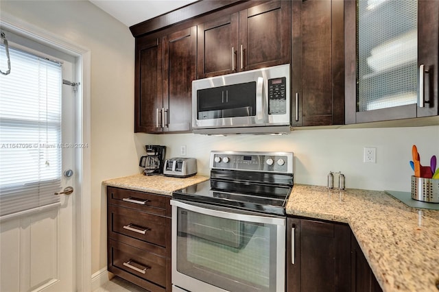 kitchen with a wealth of natural light, stainless steel appliances, dark brown cabinets, and light stone countertops