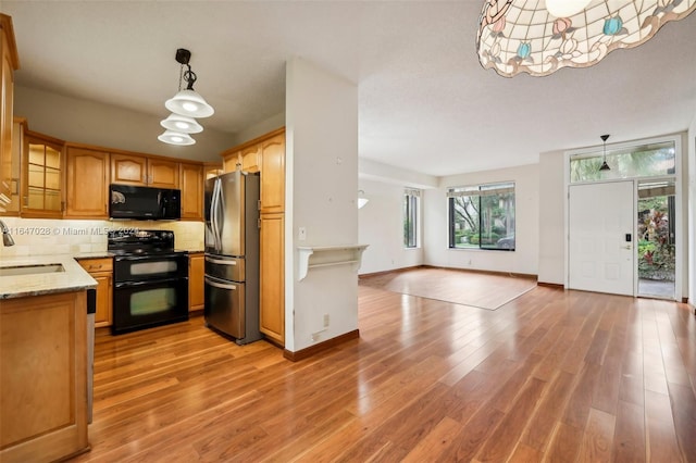 kitchen with pendant lighting, black appliances, decorative backsplash, light stone countertops, and light hardwood / wood-style floors