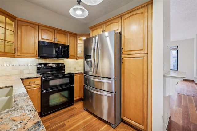 kitchen with pendant lighting, backsplash, black appliances, light stone countertops, and light hardwood / wood-style floors