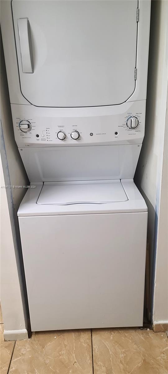 laundry area with stacked washer / dryer and light tile patterned floors