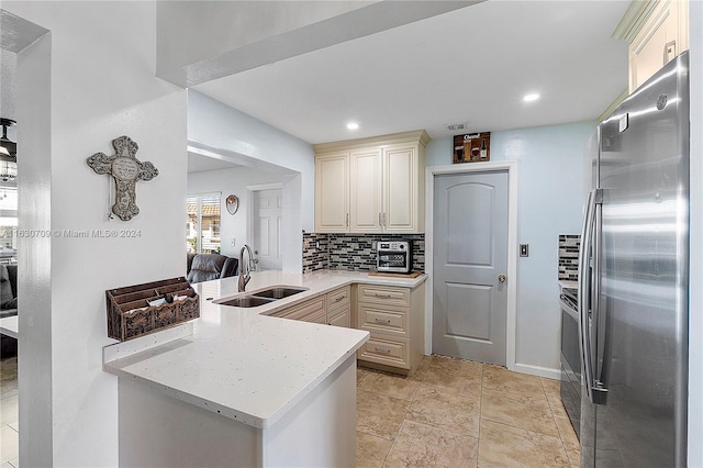 kitchen featuring backsplash, cream cabinets, sink, kitchen peninsula, and stainless steel fridge