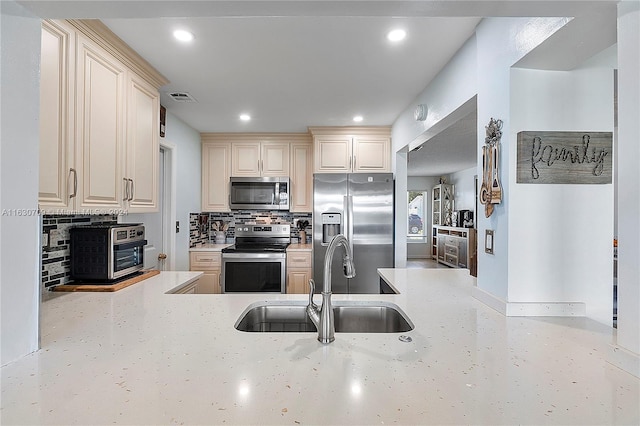 kitchen featuring decorative backsplash, appliances with stainless steel finishes, light stone countertops, cream cabinetry, and sink