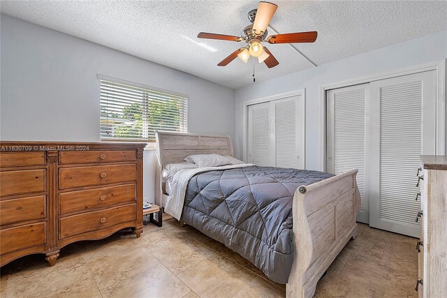 tiled bedroom featuring ceiling fan, two closets, and a textured ceiling