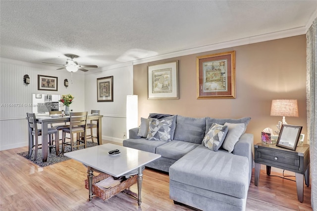 living room featuring ceiling fan, crown molding, light hardwood / wood-style flooring, and a textured ceiling