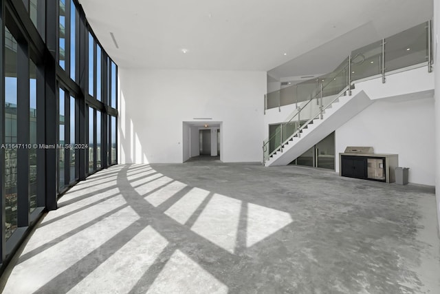 unfurnished living room with stairs, unfinished concrete floors, a towering ceiling, and expansive windows