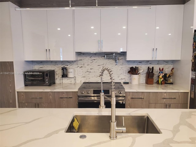 kitchen with backsplash, high end range, white cabinetry, and light stone countertops