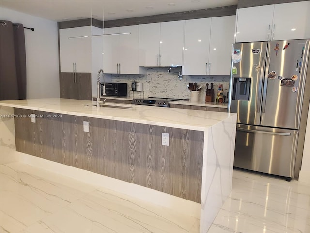 kitchen with sink, decorative backsplash, light stone counters, white cabinetry, and stainless steel fridge