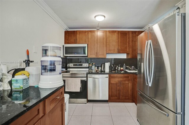 kitchen with dark stone counters, ornamental molding, tasteful backsplash, light tile patterned floors, and stainless steel appliances