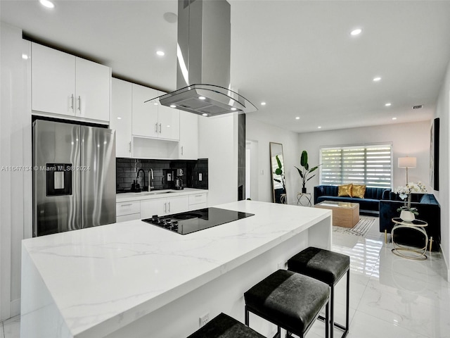 kitchen featuring island range hood, marble finish floor, black electric stovetop, stainless steel refrigerator with ice dispenser, and a sink