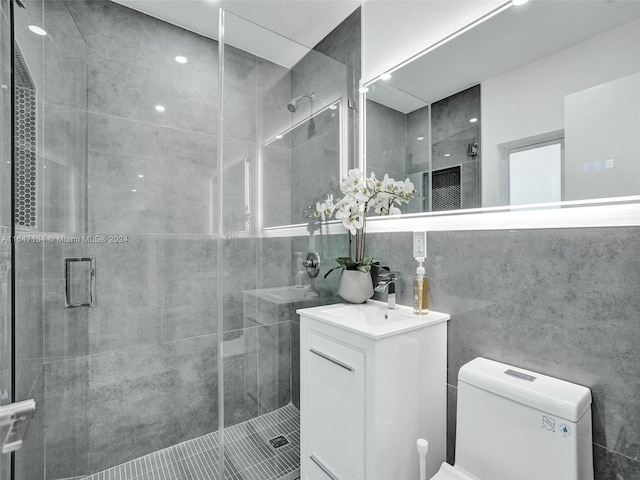 full bathroom with a stall shower, vanity, toilet, and tile walls