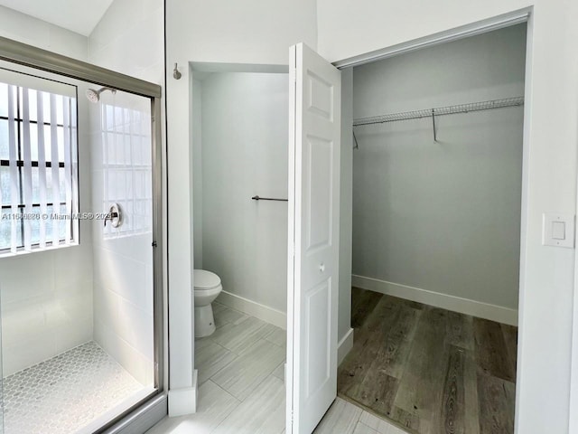 bathroom featuring wood-type flooring, a shower with shower door, and toilet