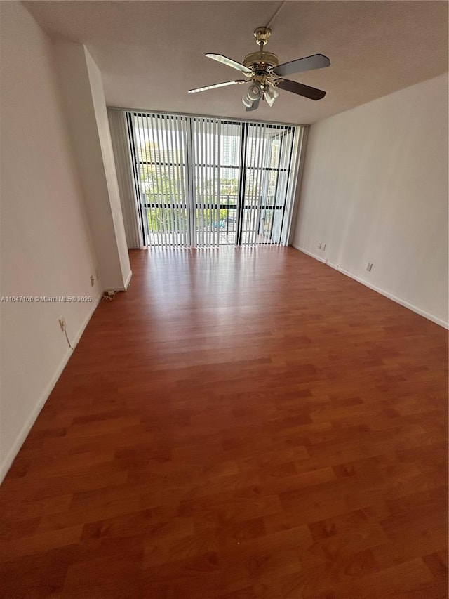 unfurnished room with wood finished floors, a ceiling fan, baseboards, and expansive windows