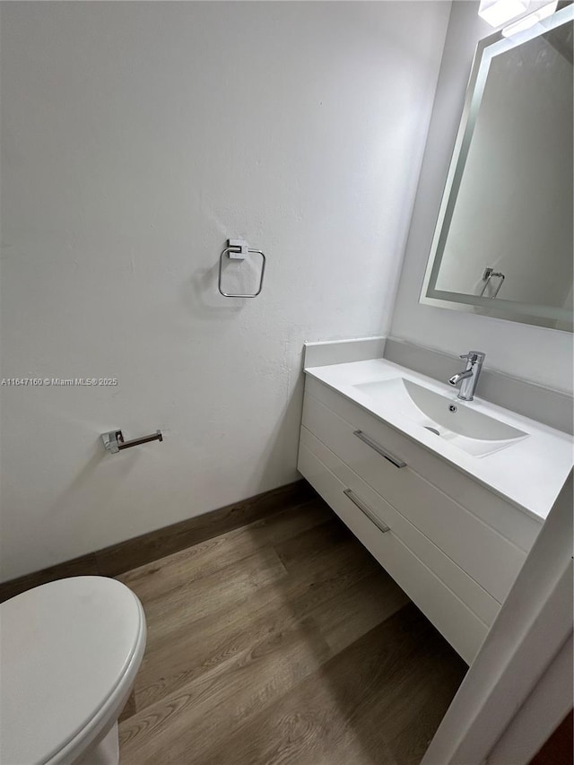 bathroom with toilet, vanity, baseboards, and wood finished floors