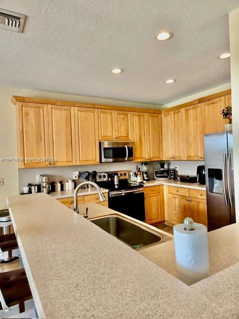 kitchen with a textured ceiling, appliances with stainless steel finishes, a breakfast bar area, and kitchen peninsula