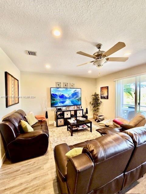 living room with a textured ceiling, light hardwood / wood-style floors, and ceiling fan