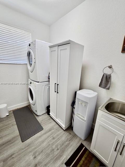 clothes washing area featuring stacked washer / drying machine, sink, and light hardwood / wood-style floors