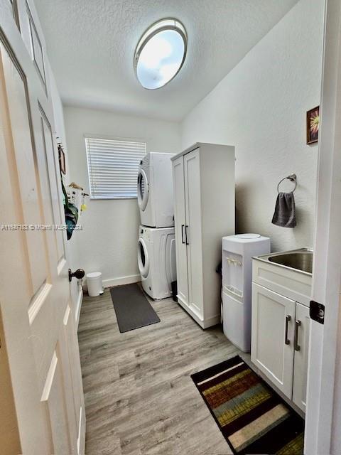 clothes washing area featuring light hardwood / wood-style floors, stacked washing maching and dryer, and sink