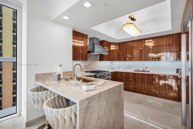 kitchen featuring wall chimney exhaust hood, kitchen peninsula, a raised ceiling, and tasteful backsplash