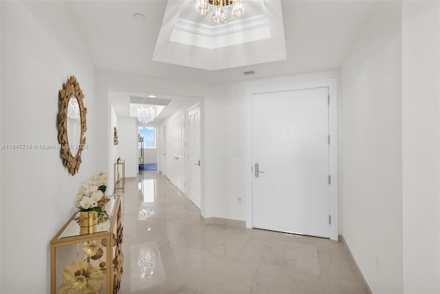 hall featuring a notable chandelier and a raised ceiling