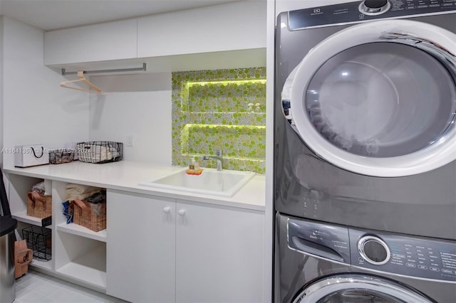 clothes washing area featuring stacked washer / drying machine, sink, and cabinets