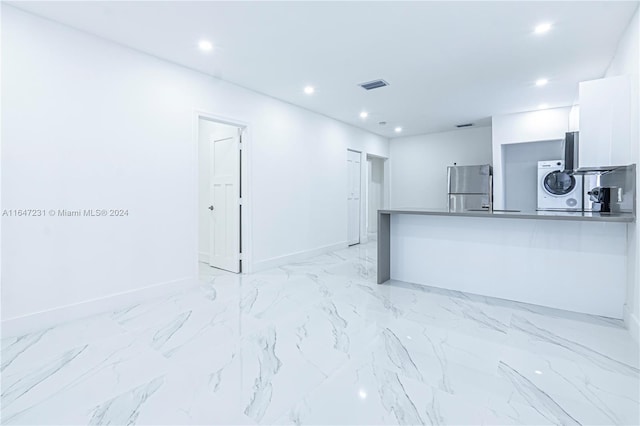 kitchen with stainless steel fridge, white cabinetry, kitchen peninsula, and stacked washer / dryer