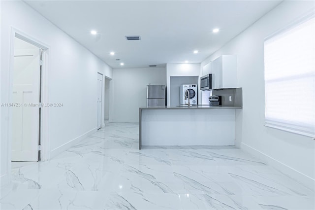 kitchen featuring white cabinets, a wealth of natural light, kitchen peninsula, stacked washer / dryer, and stainless steel appliances