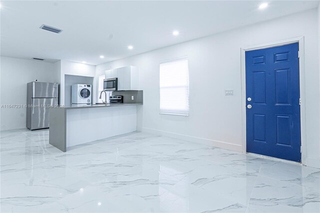 kitchen with white cabinetry, sink, stainless steel appliances, kitchen peninsula, and stacked washer and dryer