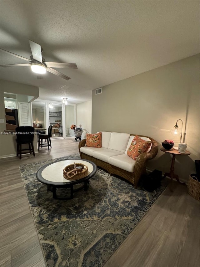 living room featuring ceiling fan, hardwood / wood-style flooring, and a textured ceiling