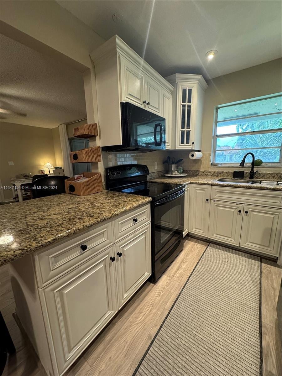 kitchen featuring sink, white cabinets, black appliances, and light stone countertops