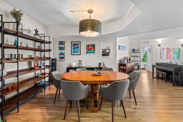 dining area with light wood-type flooring, a textured ceiling, and a raised ceiling