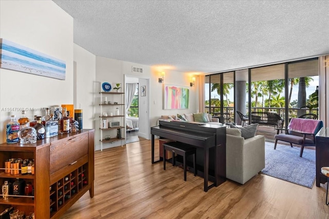 living room with expansive windows, visible vents, a textured ceiling, and light wood-style flooring