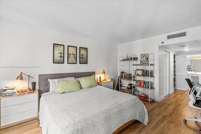 bedroom featuring baseboards, a textured ceiling, visible vents, and wood finished floors