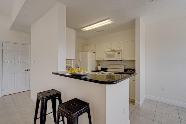 kitchen featuring kitchen peninsula, white appliances, light tile patterned floors, and a breakfast bar area