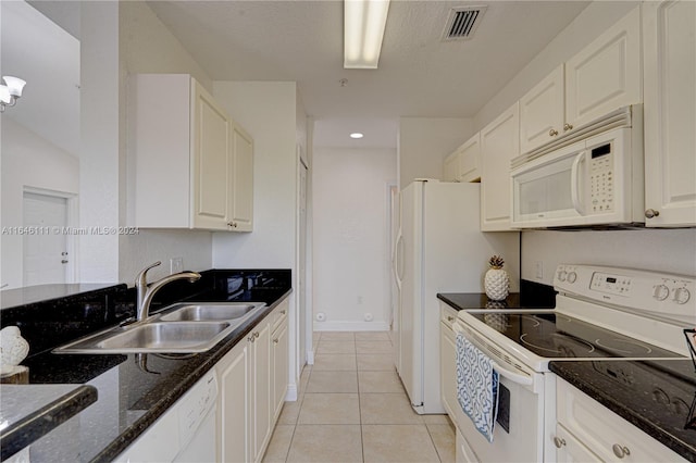 kitchen with dark stone counters, white cabinets, light tile patterned floors, sink, and white appliances