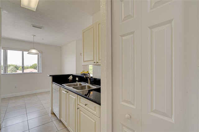 kitchen with light tile patterned floors, cream cabinetry, sink, and dishwashing machine