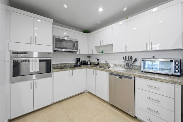 kitchen featuring white cabinets, stone countertops, appliances with stainless steel finishes, and light tile patterned flooring