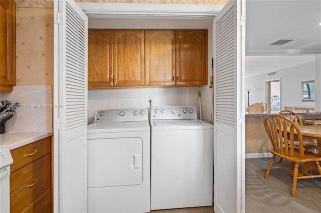 clothes washing area featuring light hardwood / wood-style floors, washer and clothes dryer, and cabinets