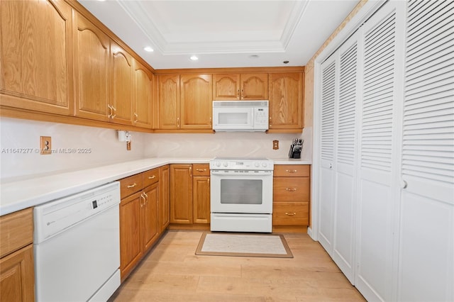 kitchen with recessed lighting, a raised ceiling, light countertops, light wood-type flooring, and white appliances