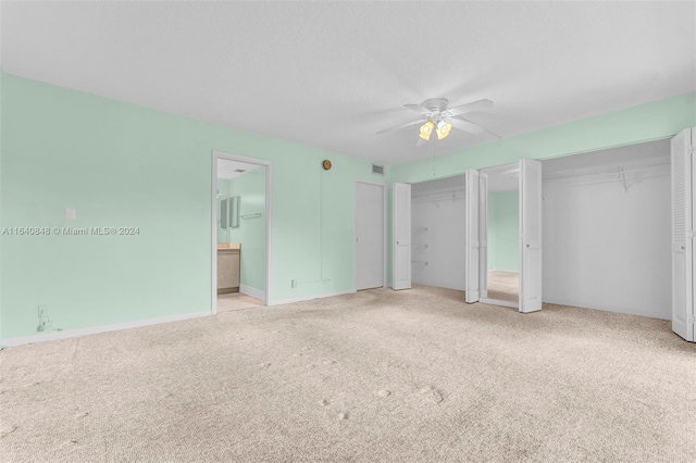 unfurnished bedroom with ensuite bath, multiple closets, a textured ceiling, ceiling fan, and light colored carpet