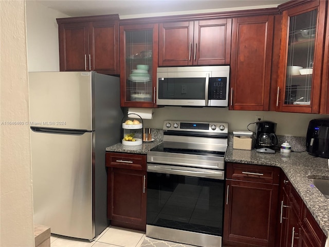 kitchen featuring appliances with stainless steel finishes, light tile patterned floors, and dark stone counters